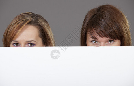 两名女在空白纸面广告牌的空边上偷看图片