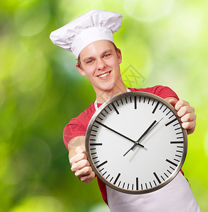 在自然背景下手持时钟的年轻厨师肖像图片