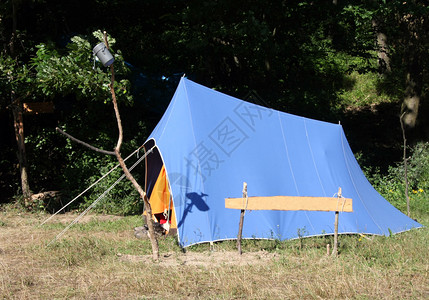营地里的蓝色帐篷Messkit在酒吧顶部的帐篷前帐篷旁边的木制信息表图片