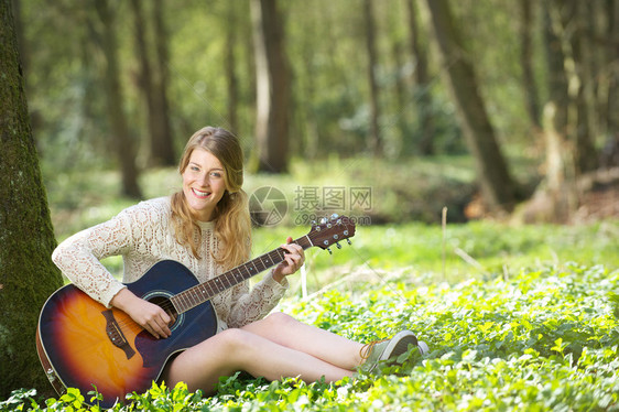 一位在户外弹吉他快乐的年轻女图片