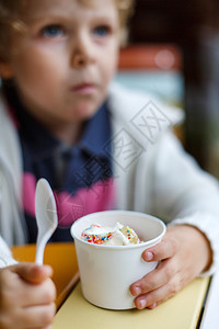 在市咖啡厅吃冰冻酸奶冰淇淋的可爱小男孩选择地把重点图片