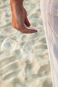 在海滩上赤脚行走的男子手握着两杯眼镜图片
