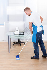 英俊的男清洁工或清洁工用拖把清洁办公楼的地板图片