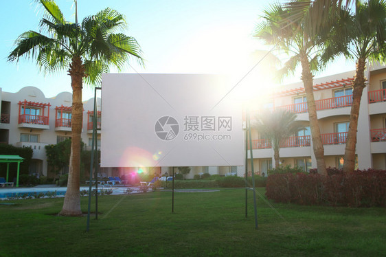 太阳在空城市广告牌后闪耀在公寓街区前的绿草坪上站在棕榈图片
