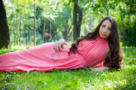 穿着粉红裙子的年轻美女长发摆在公园里躺在草地上森图片