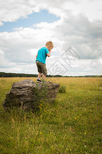 小男孩在石头上的领域中间孩子从石头上跳下来男孩图片