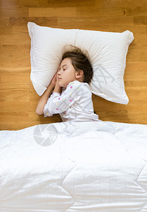小女孩睡在木制地板上白色的枕头上图片