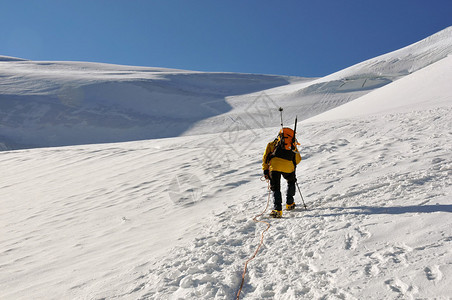 一条绳子上的登山者在高山上向着陡峭的冰川前进前面图片
