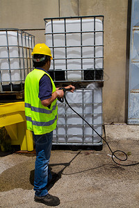 身戴硬帽和安全背心的男工人在工业环境中用塑料容器在铁窗后图片