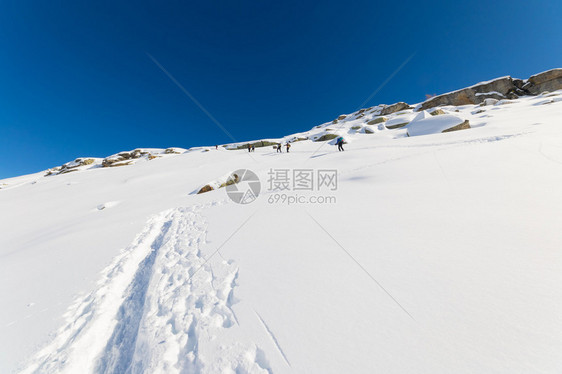 一群旅游滑雪者在陡峭的雪坡上徒步上山图片