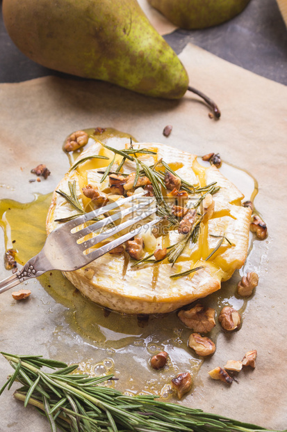 叉子上的一块烤卡芒贝尔美味的烤奶酪配蜂蜜核桃香草和梨图片