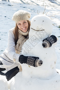 冬季快乐的年轻女子在公园里拥抱雪人白种女图片