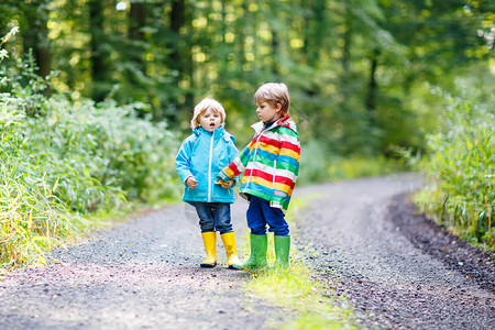 两个小兄弟穿着多彩防水雨衣和橡皮靴在秋天的森图片