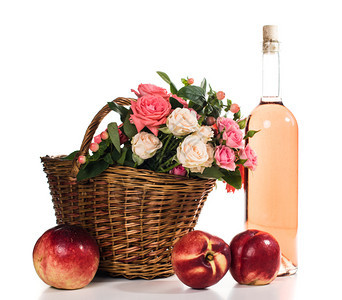 柳条篮中的新鲜天然粉红玫瑰和孤立的白色背景上的一瓶玫瑰酒水图片
