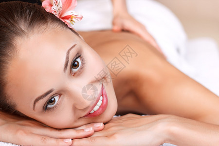 近距离接近快乐的年轻女子微笑和按摩时躺在温泉美容院里图片