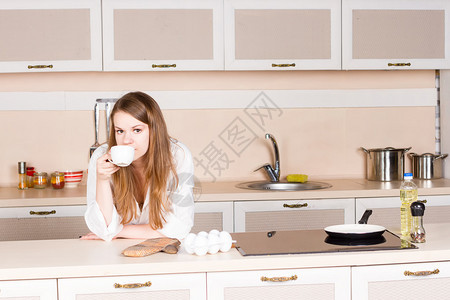 穿着白人男子长发的衬衫的女孩在厨房肘部喝茶早上在桌图片