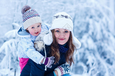 一个小女孩和她年轻美丽的母亲在雪花的雪林中戴着冬帽的肖像在寒冷的日子里与孩子们一起在户外冬季休背景图片