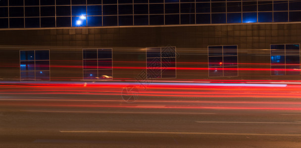 汽车在夜间穿过反射大楼时创造明亮的红色灯光小路图片
