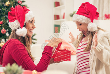 美丽的年轻母亲在圣诞节或新年给可爱的小女孩送礼物时图片