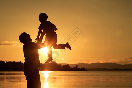父亲和儿子在日落时的山上湖边玩耍图片