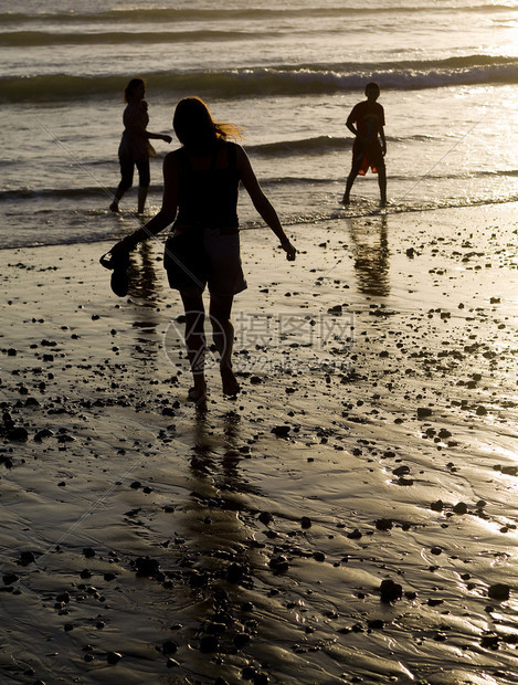 日落时在沙滩上玩耍的母亲和两个孩子剪影图片