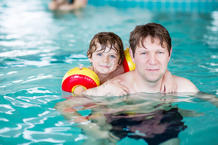年轻父亲教小儿子在室内游泳池游泳图片