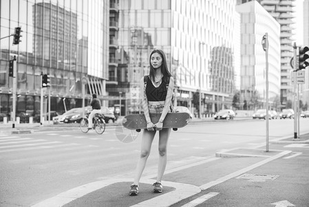 年轻英俊的亚洲长棕色直发女子滑冰运动员在城市里摆着溜冰鞋图片