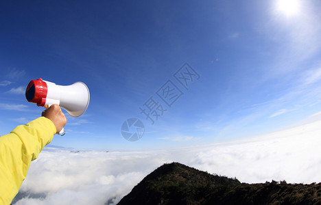 手握扬声器在山峰的蓝天上图片