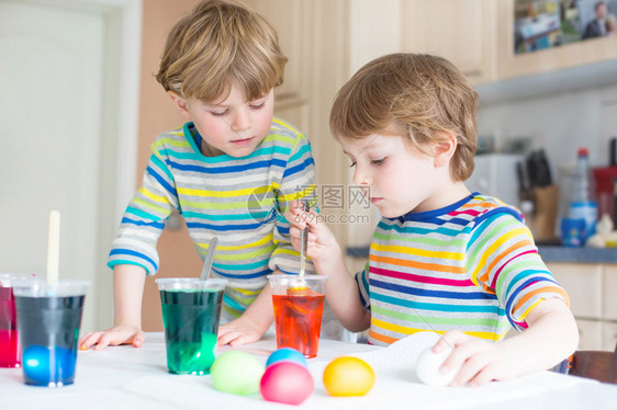 两个金发小男孩在室内厨房里为复活节假期着色鸡蛋孩子们玩得开图片