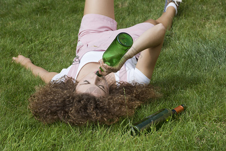 女孩啤酒瓶在公园的草地上铺图片
