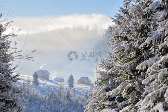 几座房屋坐落在覆盖着雪的山坡上背景中有蓝天云雾山从烟囱冒出的烟冬天阳光明媚图片