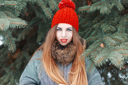 绿色云杉背景上一位红唇和红色针织帽的漂亮年图片