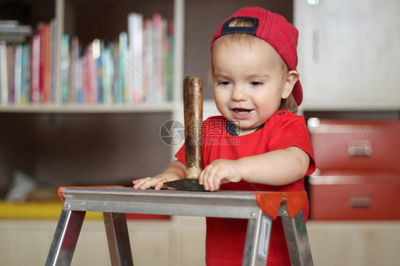 英俊的幼儿男孩握着锤子站在阶梯上室内肖图片