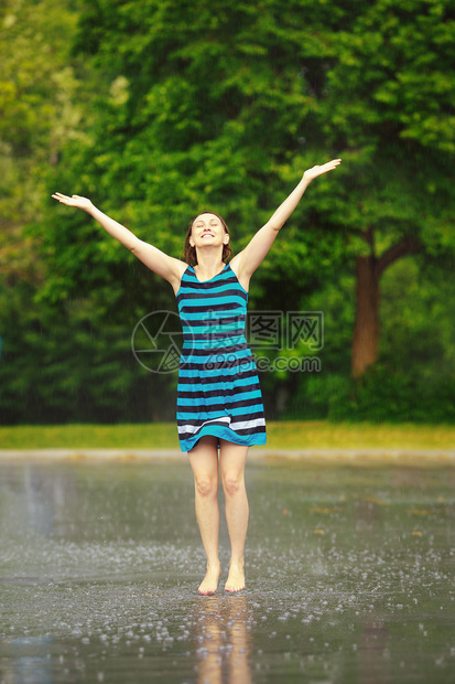 穿着蓝色连衣裙的快乐年轻白人女孩在雷雨中跳水坑的肖像图片