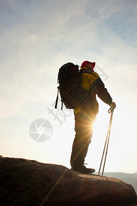手拿红帽和两极的游客的剪影背着大背包的徒步旅行者站在岩石上阳光明媚的春天破背景图片