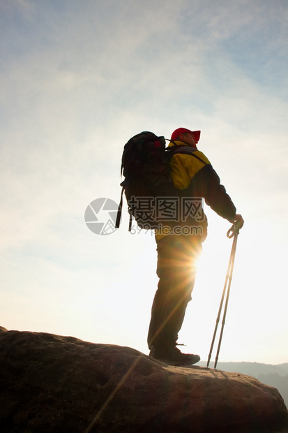 手拿红帽和两极的游客的剪影背着大背包的徒步旅行者站在岩石上阳光明媚的春天破图片