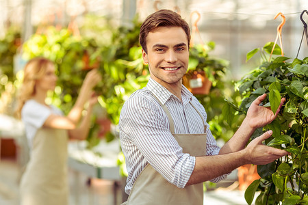 穿着围裙的美丽年轻男女在照顾橙色植物时笑着微笑男图片