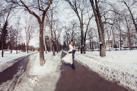 优雅时尚的新郎在白雪皑的公园举起手新娘图片