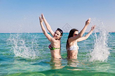两个穿着泳衣和墨镜的年轻美女在热天冲进大海图片