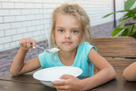 六岁女孩在院子里的木桌上吃粥图片
