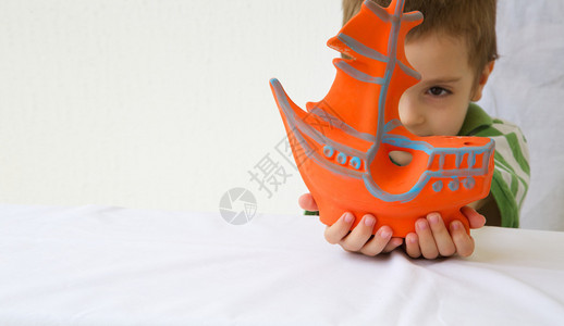 一个四岁的小男孩正在看由他制造的一条粘土橙色船图片