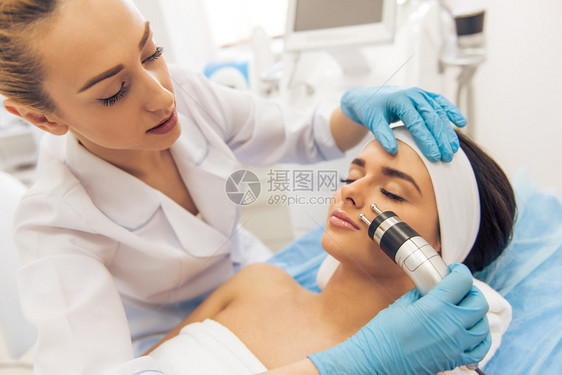 美丽的年轻女子正在接受面部皮肤治疗戴医用手套的医生正在使用现代图片