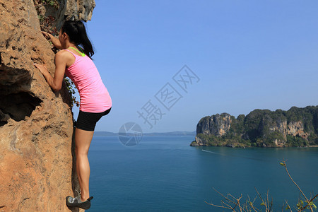 在海边山岩壁上攀登的女子攀岩者图片