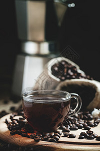 玻璃杯中的热浓咖啡咖啡豆散落在旧木桌上咖啡机深色调图像图片