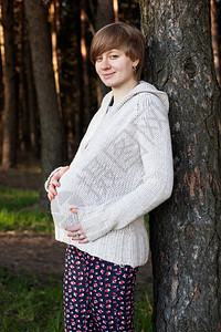 孕妇摸着肚子站在春天森林里的图片