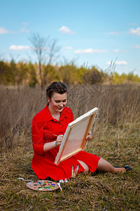 年轻艺术家画着一幅风景穿着红礼服的女图片