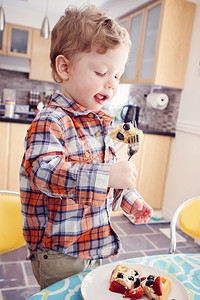 一个快乐的男孩子在清晨阳光明媚的厨房吃早餐华夫饼和水果及叉图片
