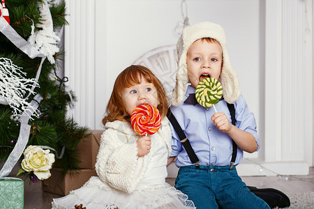 小孩吃棒糖两个有趣的小孩手里拿着美味的糖果的画像快乐的孩子和家人期待图片