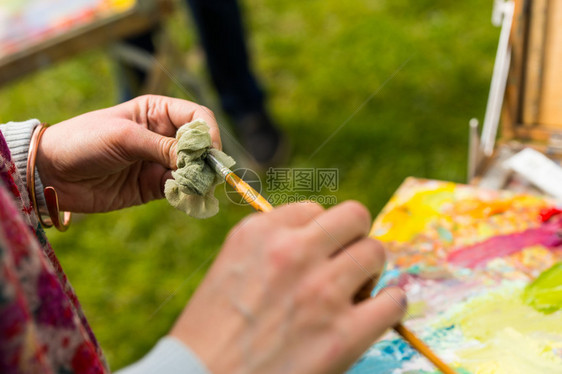 职业女画家在户外的画布上工作用抹布洗图片