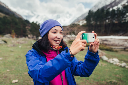 年轻女子徒步旅行者在山上与智能手机拍图片